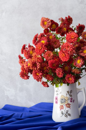 Beautiful bouquet of autumn orange chrysanthemum flowers in a vase on a blue tablecloth, part of the fall home interiorの写真素材