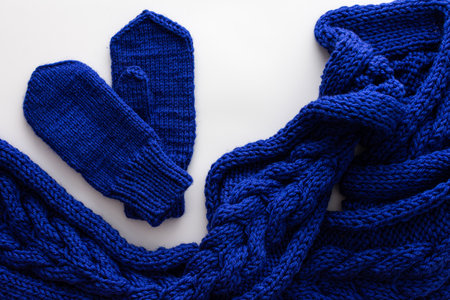 Blue knitted woolen scarf and mittens on a white background, homemade needlework concept, top viewの写真素材