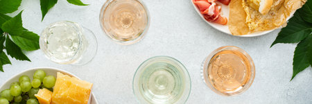 Top view of table with rose and white wine in glasses, plates with grapes, cheese and jamon, baked camembert cheese and baguette, tasting party or cozy dinner with wine bannerの写真素材