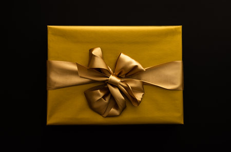 Gift box in a golden wrapper with a bow close-up on a black backgroundの写真素材
