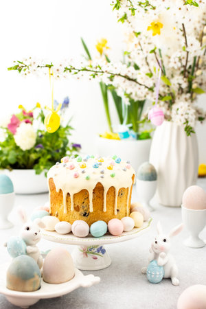 Easter home interior, Easter cake with eggs on the background of a vase with blossoming cherry branches and bouquets of flowers, cute bunniesの写真素材