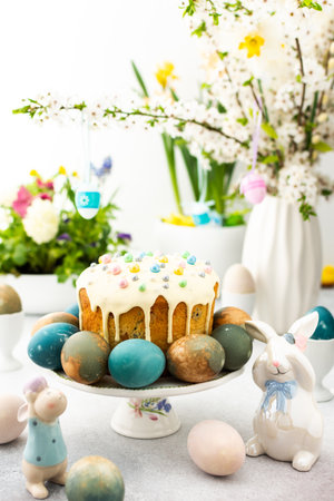 Easter home interior, Easter cake with eggs on the background of a vase with blossoming cherry branches and bouquets of flowers, cute bunniesの写真素材