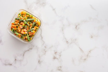 Frozen mix of vegetables in a container close-up, frozen asparagus beans and peas, corn and carrots, copy space, top viewの写真素材