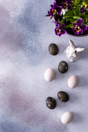 Colorful Easter eggs and cute bunnies on a pastel pink background, pansies in a pot, top view, copy spaceの写真素材