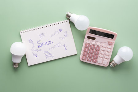 Save energy, accounting and saving money, energy saving light bulbs and notebook on a green background, money spending planning, rising electricity costs, energy crisis in Europeの写真素材