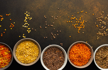 Multi-colored lentils in bowls on a brown background, scattered yellow and brown, green and orange lentils, healthy legumes, top viewの写真素材
