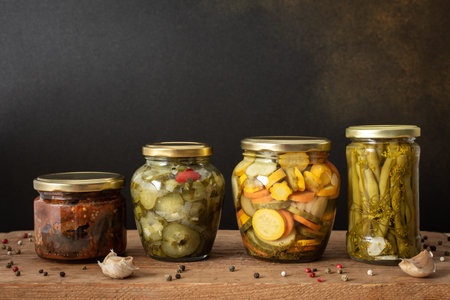 Preserving vegetables for the winter, canned vegetables in jars on a wooden table against a brown wall, pickled or fermented vegetables, copy spaceの写真素材