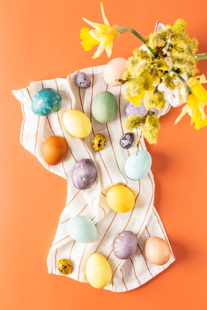 Top view of napkin with dyed natural dyes Easter eggs, bouquet with yellow daffodils in vase on orange backgroundの写真素材