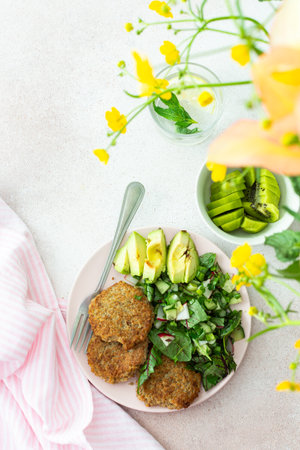 Quinoa cutlets and mixed salad with avocado and radishes, kiwi and water with lemon, delicious hearty breakfasts, a set table with food and a vase of flowers, vegan lunch plateの写真素材