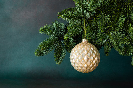 Golden Christmas ball hanging on a fir branch on a green background, Christmas backgroundの写真素材