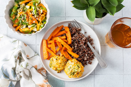 A delicious and wholesome plate featuring brown rice, sweet potatoes, and chickpea pancakes made with squash, perfect for a balanced and nutritious meal, fresh salad of tomatoes cucumbers with herbsの写真素材