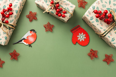 Christmas festive background, gift boxes with a sprig of rowan and red stars, a bullfinch and a mitten on a green background, top viewの写真素材
