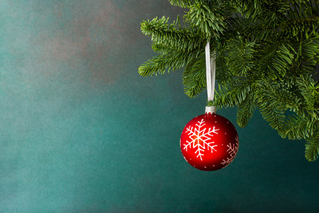 Red ball with snowflakes hanging on a Christmas tree branch on a green background, Christmas backgroundの写真素材