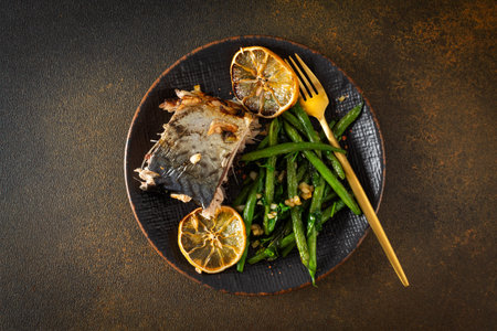 This savory dish features baked green beans with onions and tender mackerel, served on a plate with a brown background, offering a balanced and flavorful gourmet mealの写真素材