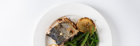 Enjoy a delicious and nutritious meal of baked green beans with onions and baked mackerel, beautifully presented on a plate against a white background, perfect for dinner, bannerの写真素材