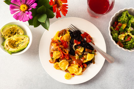 A nutritious and delicious breakfast plate featuring black rice with stewed vegetables, fresh tomato-broccoli-radish salad, avocado with sesame seedsの写真素材