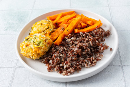 A delicious and wholesome plate featuring brown rice, sweet potatoes, and chickpea pancakes made with squash, perfect for a balanced and nutritious meal, fresh salad of tomatoes cucumbers with herbsの写真素材