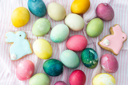 Multi-colored Easter eggs with decorative bunnies on a pink tablecloth, top view, Happy Easter holidayの写真素材