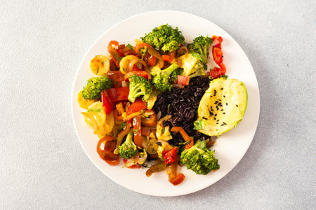 A hearty and nutritious breakfast of black rice with stewed vegetables like tomatoes, zucchini, peppers, and onions, fresh salad with tomatoes, broccoli, and radish, avocado with sesame seedsの写真素材