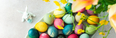 Multi-colored Easter eggs in an oval dish with decorative bunnies and tulip, top view, Happy Easter holidayの写真素材