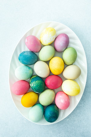Multi-colored Easter eggs in an oval dish on a blue background, top view, Happy Easter holidayの写真素材