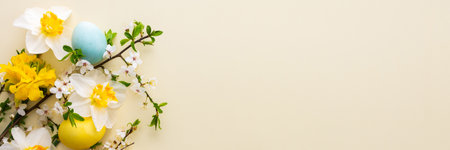 Festive banner with spring flowers and Easter eggs, white daffodils and cherry blossom branches on a yellow pastel backgroundの写真素材