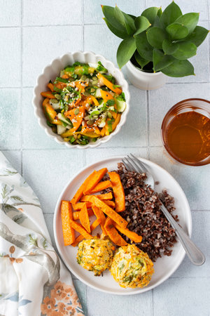 A healthy and filling meal of brown rice, baked sweet potato and squash chickpea pancakes, packed with flavor and nutrients, fresh salad of tomatoes and cucumbers with herbsの写真素材