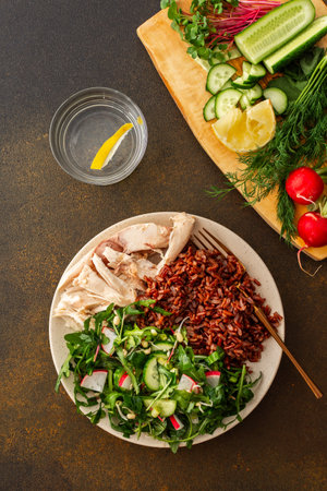 Delicious healthy breakfasts, chicken breast with red rice and salad mix with fresh seasonal organic vegetables and microgreens, top view of a plate with food and a cutting board with vegetablesの写真素材