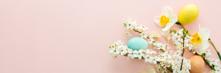 Festive banner with spring flowers and Easter eggs, white daffodils and cherry blossom branches on a pink pastel backgroundの写真素材