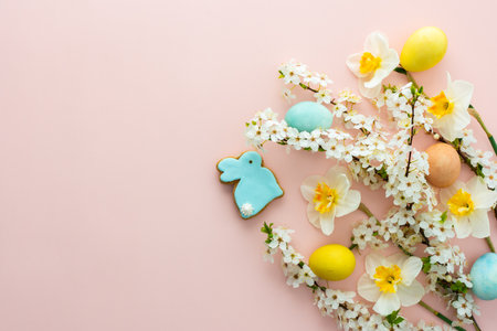 Festive background with spring flowers and naturally colored eggs and Easter bunnies, white daffodils and cherry blossom branches on a pink pastel backgroundの写真素材