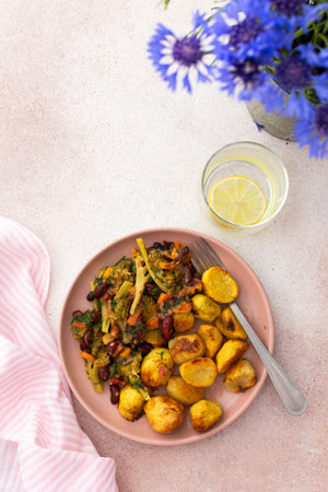 Stewed potatoes with stewed vegetables, broccoli and beans with carrots and herbs, a served table with food and a vase of flowers, a delicious hearty lunch or dinnerの写真素材