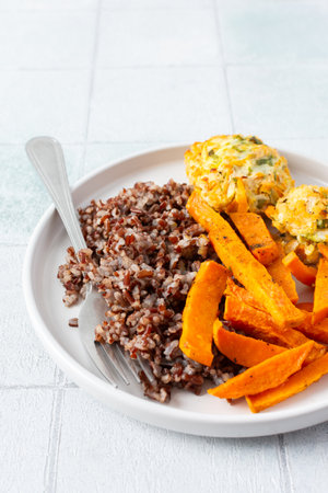 A healthy and filling meal of brown rice, baked sweet potato and squash chickpea pancakes, packed with flavor and nutrients, fresh salad of tomatoes and cucumbers with herbsの写真素材