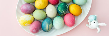 Multi-colored Easter eggs in an oval dish with decorative bunnies on a pink background, top view, Happy Easter holiday bannerの写真素材