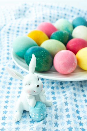 Multi-colored Easter eggs in an oval dish with decorative bunnies on a blue tablecloth, Happy Easter holidayの写真素材
