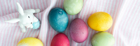 Multi-colored Easter eggs with decorative bunnies on a pink tablecloth, top view, Happy Easter holiday bannerの写真素材