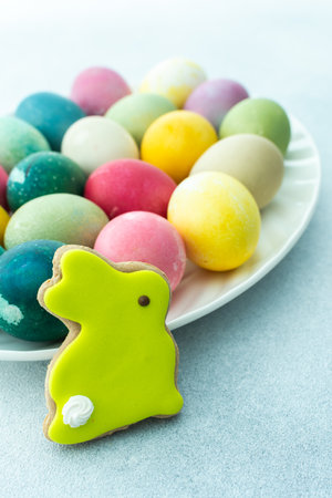 Multi-colored Easter eggs in an oval dish with decorative bunnies on a blue background, Happy Easter holidayの写真素材