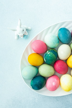 Multi-colored Easter eggs in an oval dish with a decorative bunny on a blue background, top viewの写真素材
