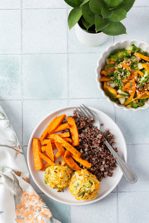 A healthy and filling meal of brown rice, baked sweet potato and squash chickpea pancakes, packed with flavor and nutrients, fresh salad of tomatoes and cucumbers with herbsの写真素材