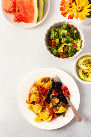 A filling breakfast of black rice with stewed tomatoes, zucchini, peppers, and onions, accompanied by a fresh salad of tomatoes, broccoli radish avocado , with watermelon for dessertの写真素材
