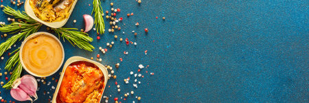 Different open tin cans with canned fish like mackerel, sprat, sardine, fish pate among spices and herbs on a blue background, viewed from the top, bannerの写真素材