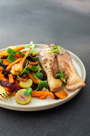 Baked silver carp with roasted carrots, zucchini, beets, and garlic , perfect for a healthy and delicious breakfast , plates with food on a dark backgroundの写真素材