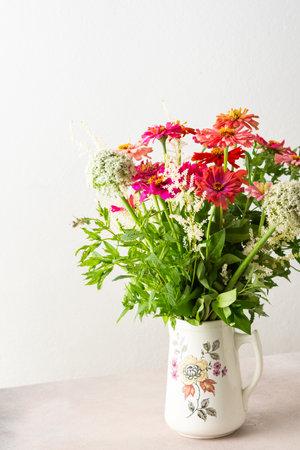 Summer bouquet of colorful Zinnia and mint sprigs, bouquet of flowers on the table near the wall, home decoration with flowersの写真素材