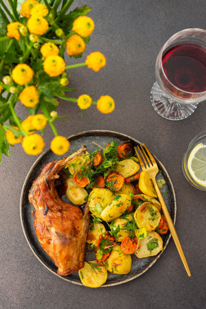 A hearty delicious dinner, baked rabbit with potatoes and carrots, a set table with food, a glass of wine and a vase of flowersの写真素材