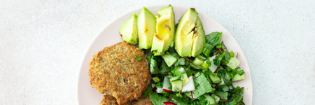 Quinoa cutlets and mixed salad with avocado and radishes, kiwi and water with lemon, delicious hearty breakfasts, vegan lunch plate bannerの写真素材