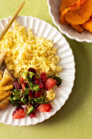 A balanced breakfast with millet, tender baked chicken breast, a refreshing salad of greens and grapefruit, and roasted sweet potatoes, offering a nutrient-packed mealの写真素材