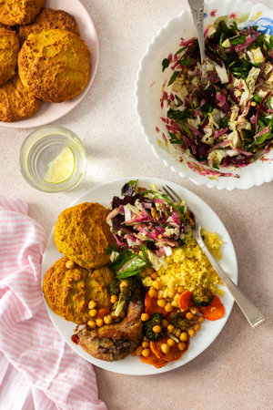 A filling, balanced breakfast with lentil and zucchini pancakes, millet, baked chicken neck, roasted sweet potatoes, broccoli, carrots, chickpeas, and a fresh salad with radish, sprouts, and nutsの写真素材