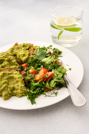 Enjoy a healthy breakfast with zucchini pancakes topped with green pea pesto, served with a mixed salad of fresh seasonal vegetables and herbs for a nutritious startの写真素材