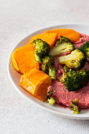 A healthy, balanced breakfast with beetroot hummus, roasted sweet potatoes, and broccoli, topped with a fresh pink radish and Chinese cabbage salad with chia seedsの写真素材