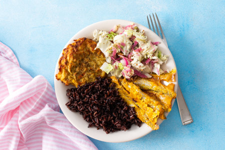A wholesome and savory breakfast with brown rice and baked white fish, complemented by zucchini-carrot pancakes and a fresh cabbage salad with radishの写真素材