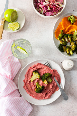 A healthy breakfast with beet hummus, baked sweet potato, and broccoli, topped with a fresh radish and cabbage salad, offering protein and nutrientsの写真素材